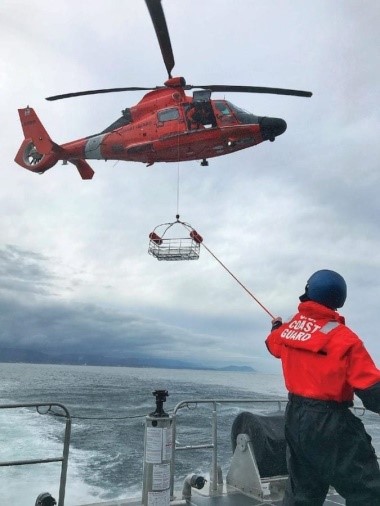 A Coast Guard MH-65D demonstrates a “trail line hoist” procedure with a small boat. Note the hypotenuse or diagonal formed by the trail line running from the person on deck to the hoist hook. (U.S. Coast Guard)